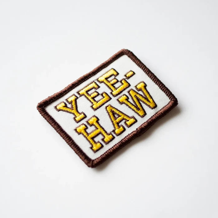 Embroidered patch with YEE HAW in bold yellow letters on white fabric with a brown edge