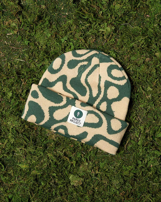 Yellowstone Geysers Beanie displayed on mossy ground in beige and green abstract pattern
