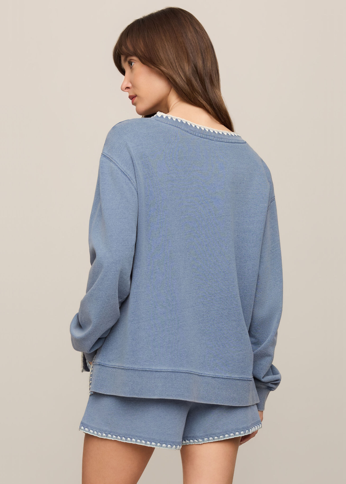 Woman turned to the side wearing a blue knit denim sweatshirt with whipstitch trim and matching shorts
