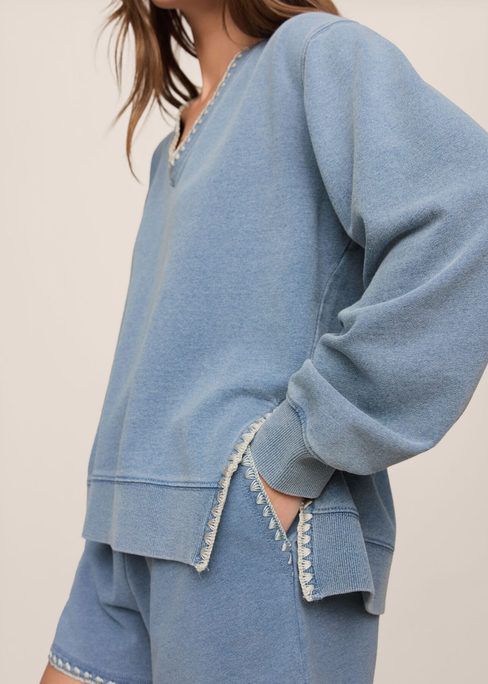 Close up of a woman wearing a blue knit denim sweatshirt with whipstitch trim and matching shorts