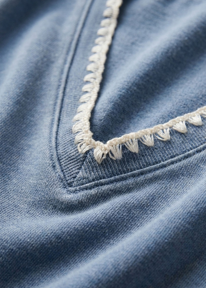 Close up of a blue knit denim sweatshirt with whipstitch trim